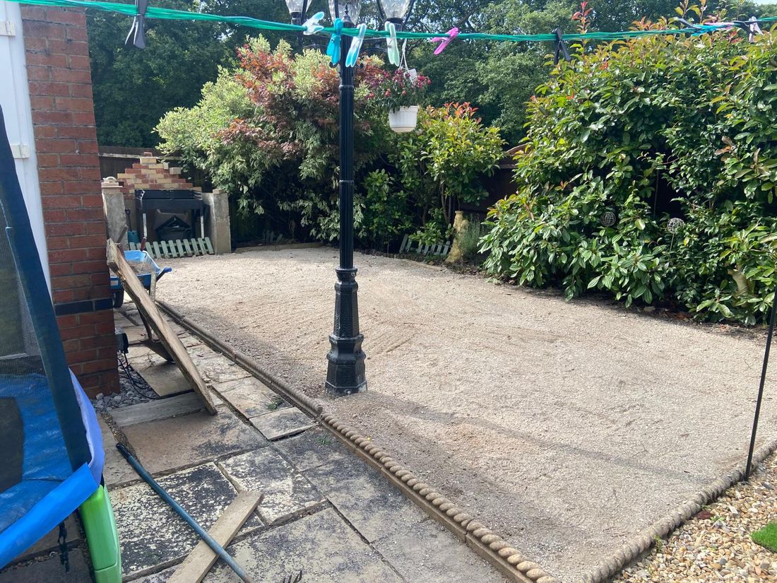 Small courtyard with a flat gravel sub-base, black lamp post, rope edging, shrubs and a brick wall behind