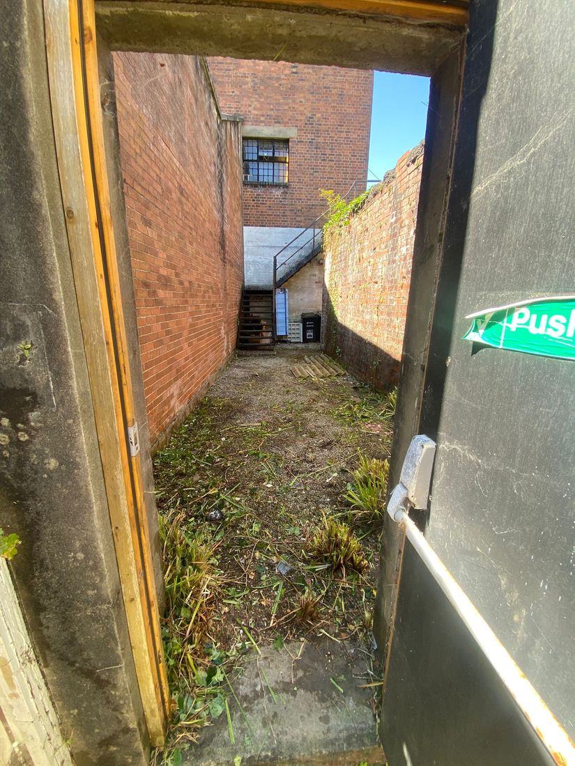 View through a doorway into a brick yard with cut weeds scattered over the ground and a staircase beyond