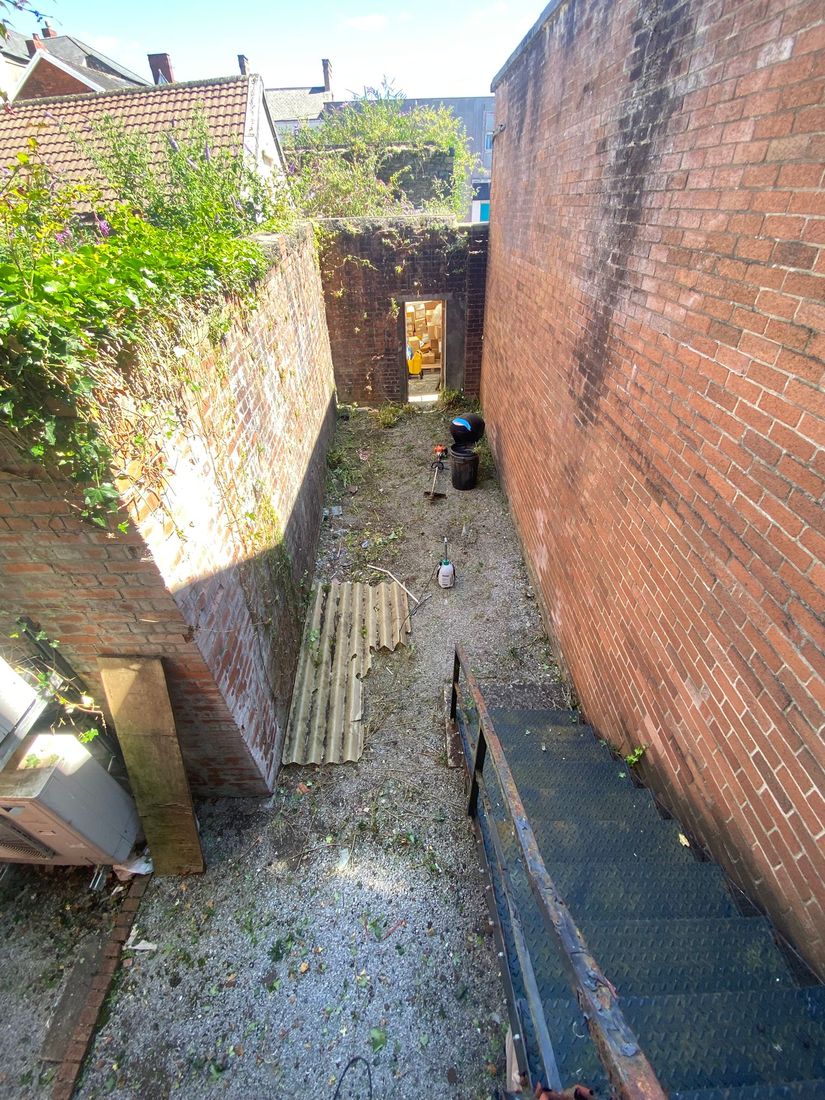 Brick-walled yard seen from above after cutting, with bare gravel, a corrugated sheet and a bin