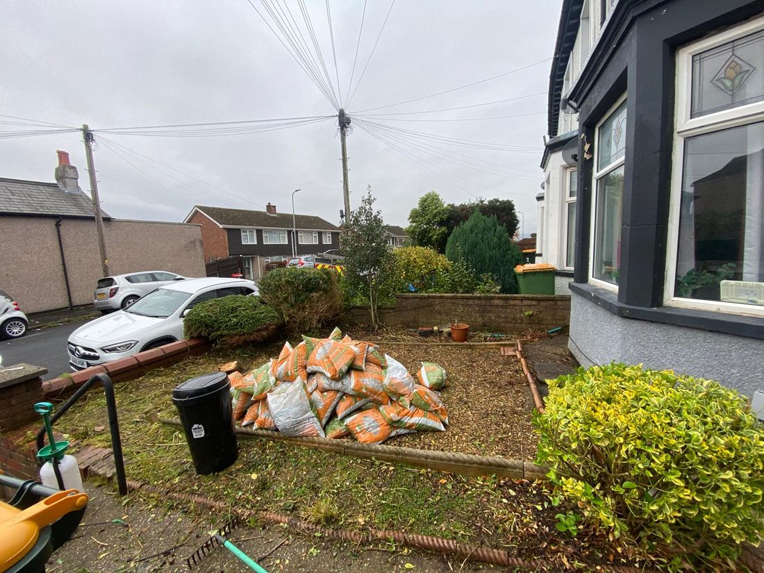 Cleared front garden with raked ground, a pile of orange bags, a bin, and hedges kept at the boundary
