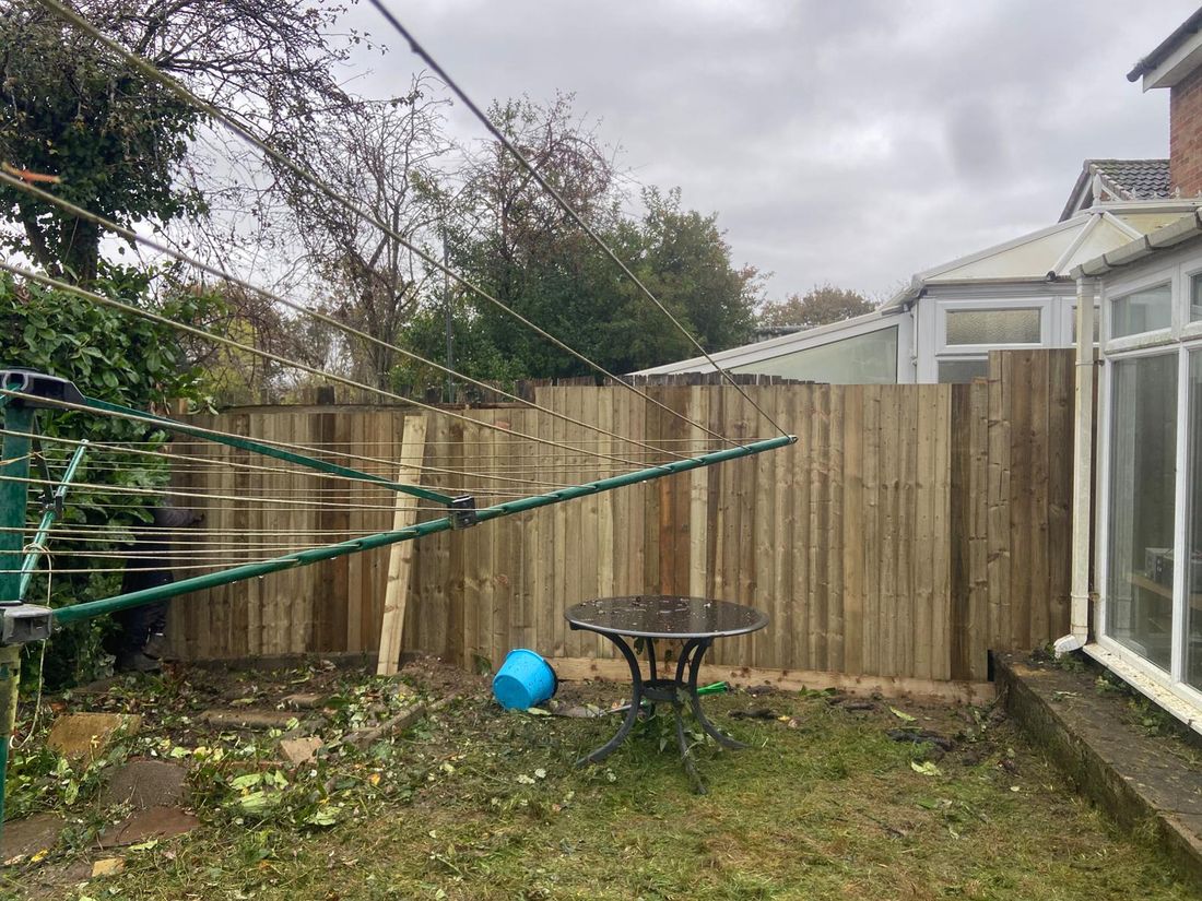 Worn grey timber fence with a pile of broken boards and a person working beside a conservatory