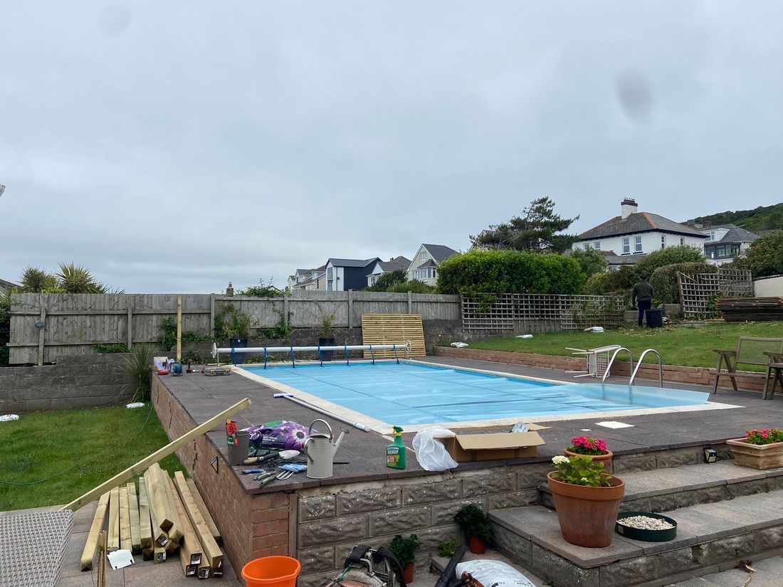 Raised garden swimming pool with stacked timber posts, tools and a new panel, and an older fence behind