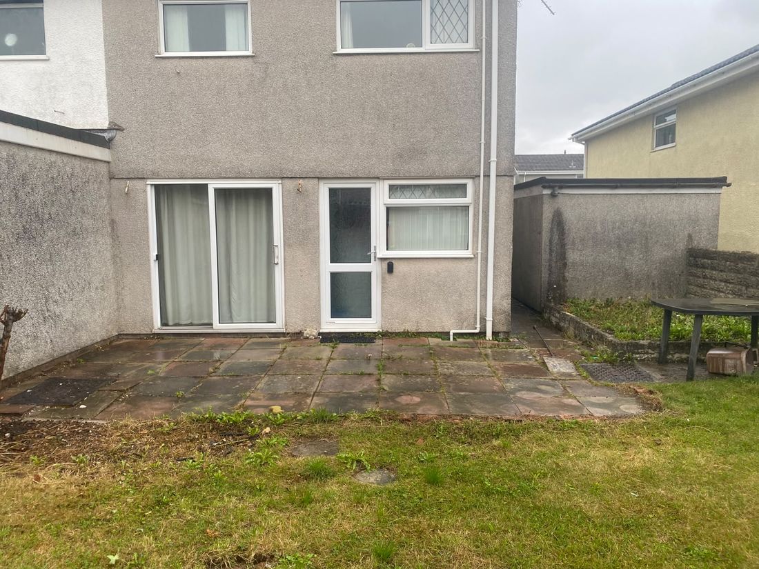 Rear of a pebble-dashed house with stained old paving slabs and a worn lawn in front