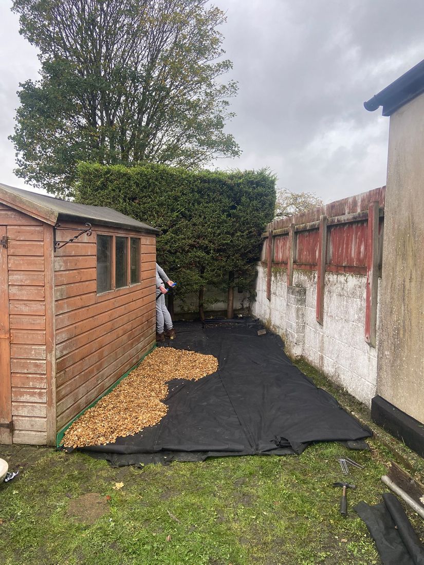 Side strip beside a timber shed covered with black weed membrane and a spread of golden gravel