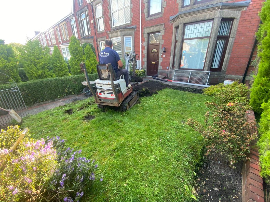 Man on a mini digger stripping the lawn in a front garden of a red brick terraced house