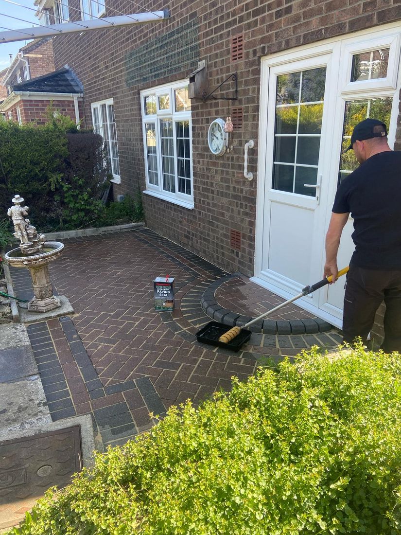 Cleaned red block paving with a man rolling seal from a tray beside a white door
