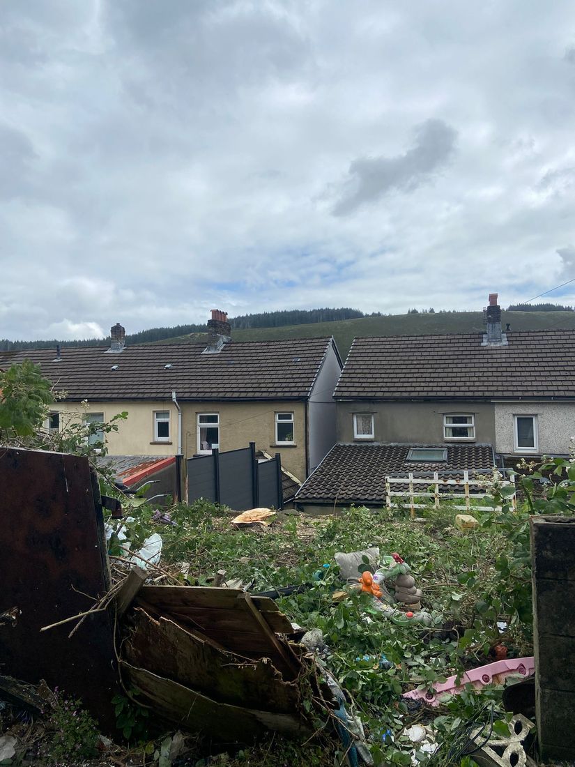Cleared back garden with scattered debris, looking over terraced houses towards a hillside