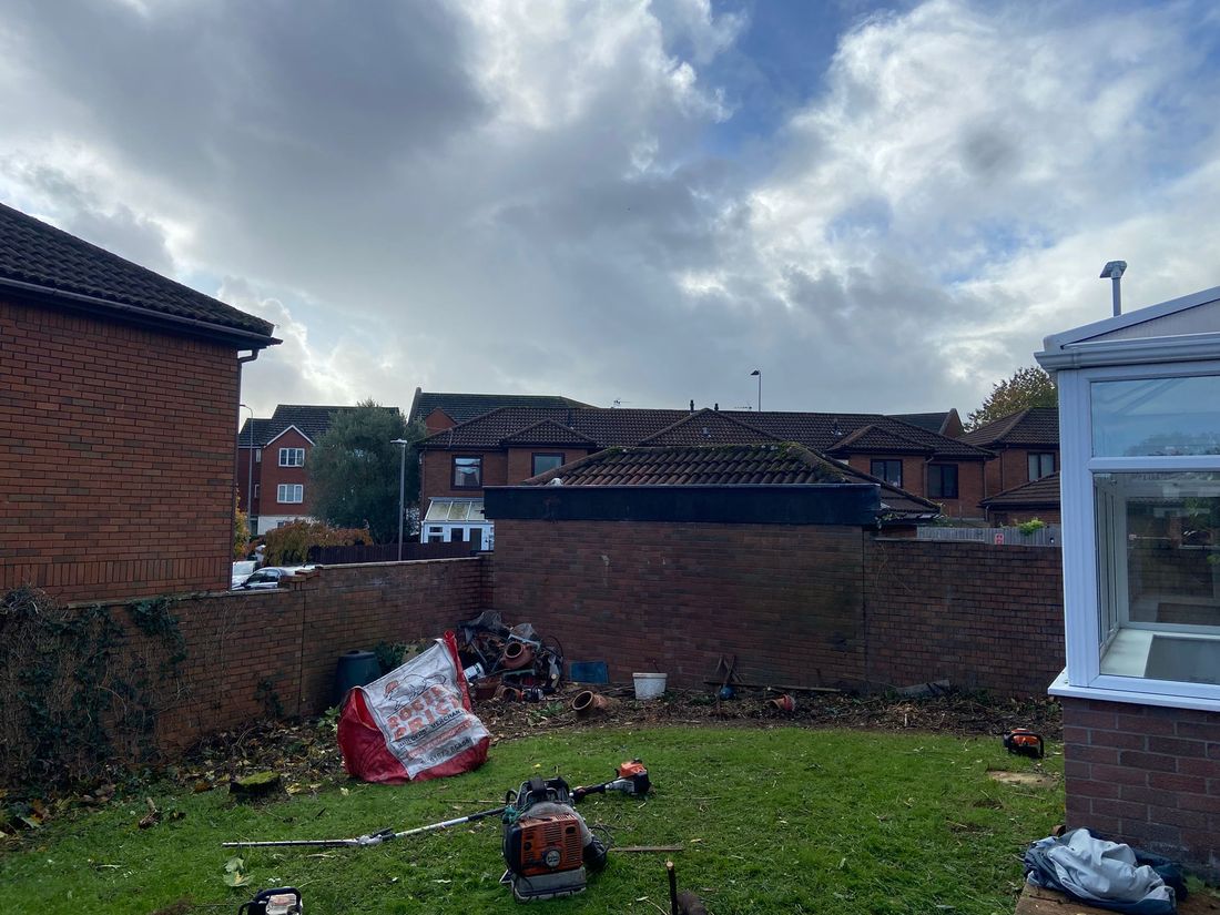 Cleared lawn enclosed by brick walls with a conservatory on the right and hedge trimmers and a blower on the grass