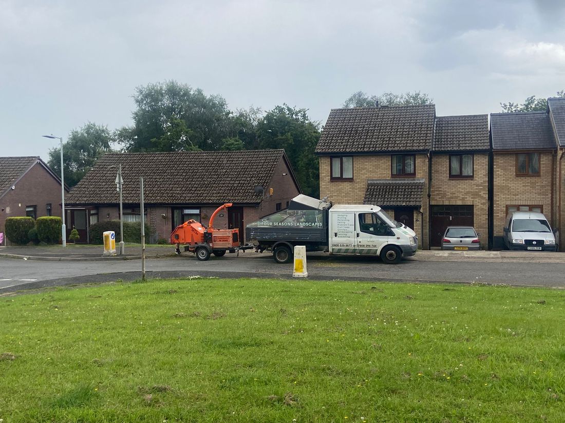 Orange wood chipper and tipper truck parked on a road beside a grassy green and houses