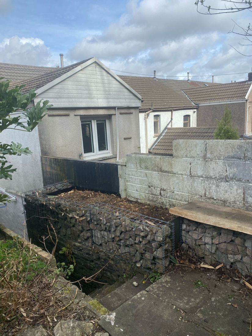 Bare stone-filled wire planter beside a block wall in a Pontypridd back garden after bamboo removal